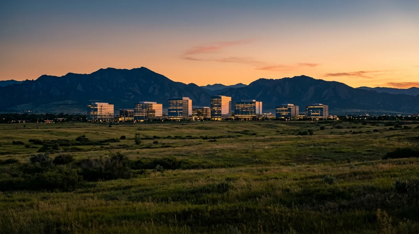 Glass office buildings at dusk in the Denver Tech Center with the foothills on the horizon